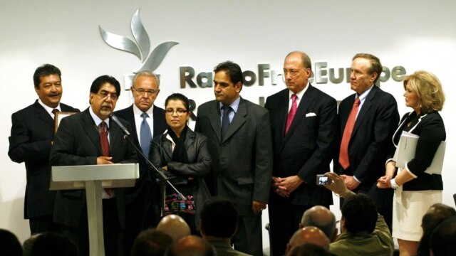 A line of David Burke Award Winners with BBG governors stand in front of a wall with the Radio Free Europe logo.