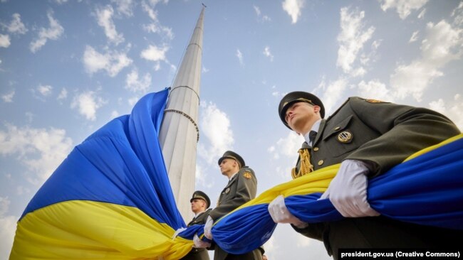 Soldiers hold a large Ukrainian flag.