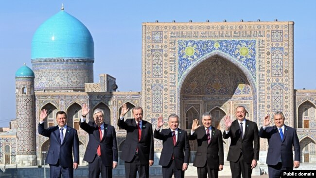 Leaders from Azerbaijan, Kazakhstan, Kyrgyzstan, Turkey, and Uzbekistan standing in a line to celebrate The Organization of Turkic States (OTS) meeting. They stand in front of an ancient building in Samarkand, Uzbekistan.