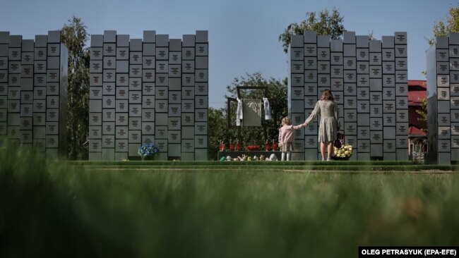 An image of a mother and young daughter holding hands at a memorial for victims of war crimes in Bucha, Ukraine, from September 2023