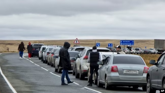 People walk next to their cars queuing to cross the border into Kazakhstan at Mariinsky border crossing after President Vladimir Putin announced a partial mobilization of reservists to fight in Ukraine. (AP Photo)