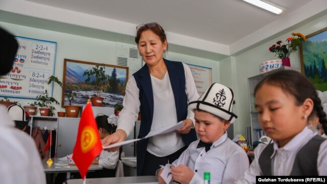 A teacher hands out papers to students in a Bishkek classroom.