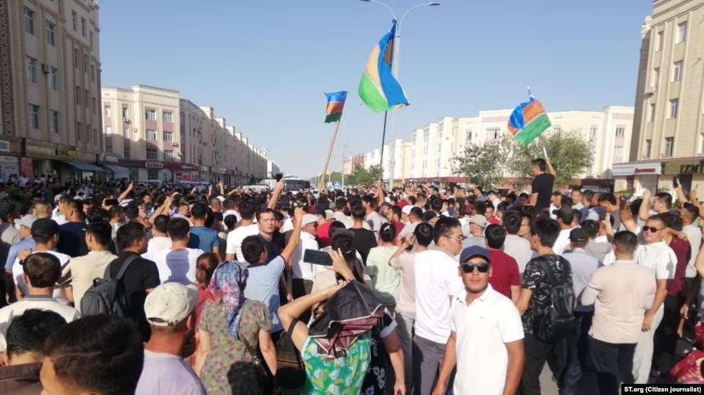 A large crowd waves flags and stands in the street for a demonstration in Karakalpakstan.