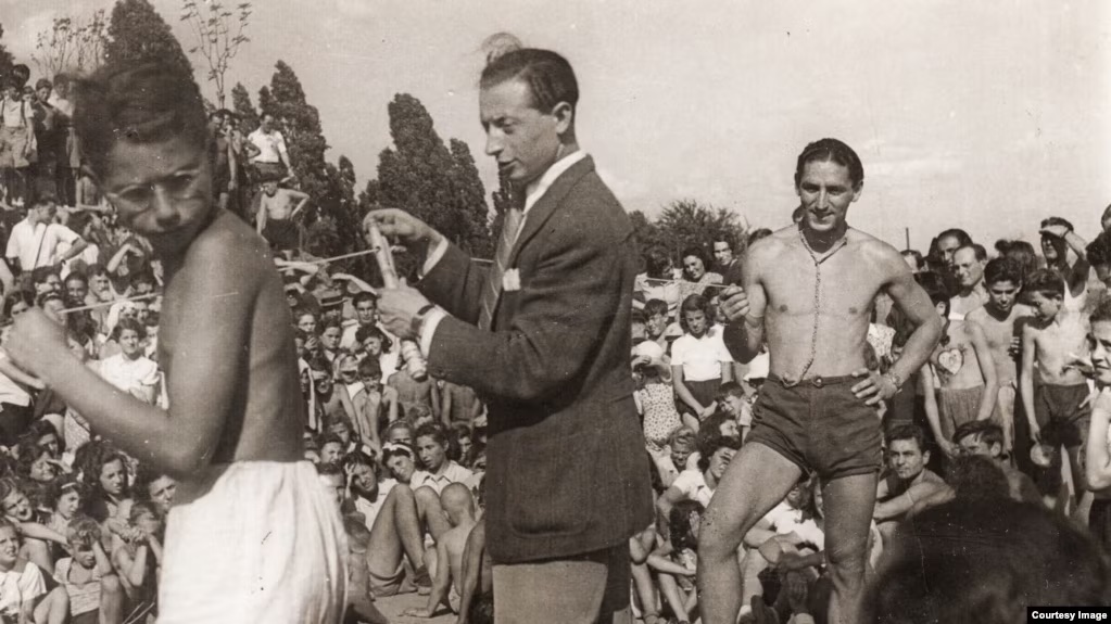 A group of young people participate in a sporting event or summer activity. To the right of the photo, Freddy Hirsch stands and watches two men preparing for a competition.